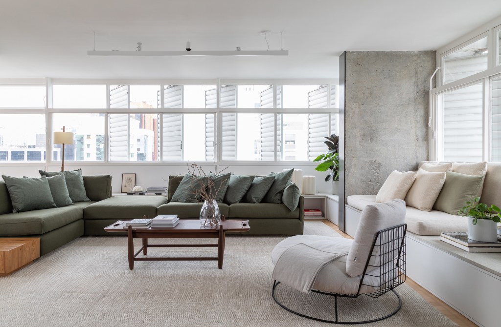 Apê dos anos 1960 é modernizado com dog shower e pilar no meio da sala. Projeto de Casa33 Arquitetura, Na foto, sala de estar com sofá verde, pilar na sala e mesas.
