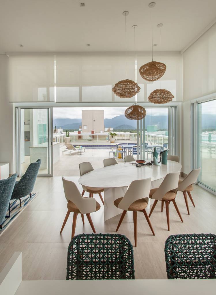 ape-decor-inspirado-praia-toques-azuis-e-porcelanato-areia-korman-arquitetos-06 Apê tem décor inspirado na praia com toques azuis e porcelanato areia. Projeto de Korman Arquitetos. Na foto, sala com pé-direito alto, persianas brancas, mesa oval, cadeiras brancas, luminária de palhinha.
