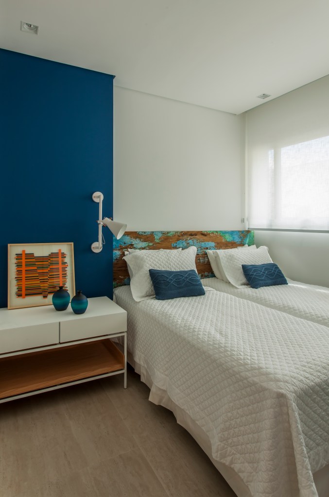 Apê tem décor inspirado na praia com toques azuis e porcelanato areia. Projeto de Korman Arquitetos. Na foto, quarto com duas camas de solteiro, cabeceira de madeira rústica.