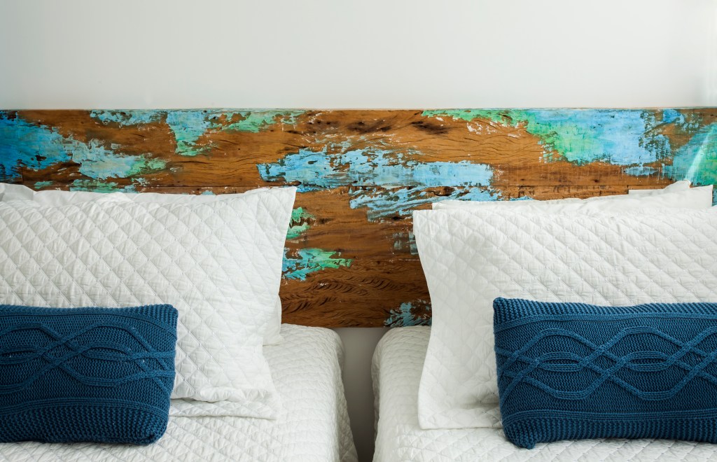 Apê tem décor inspirado na praia com toques azuis e porcelanato areia. Projeto de Korman Arquitetos. Na foto, quarto com duas camas e cabeceira de madeira rústica.