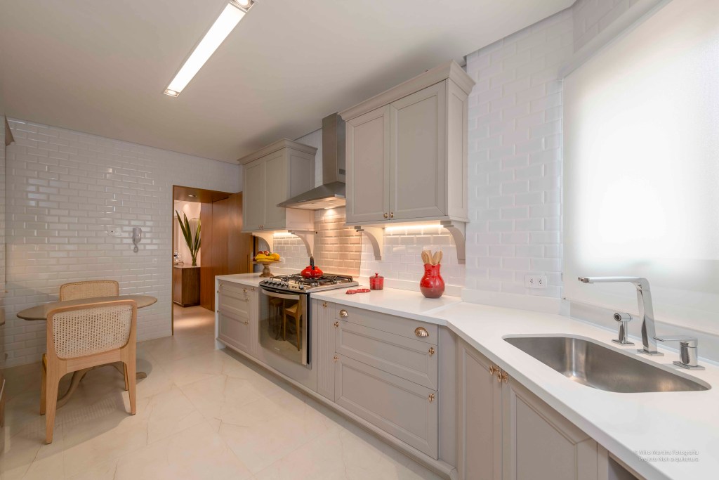 Apê ganha cozinha clássica com bancada de quartzo e armários ornamentados. Projeto de Augusto Manzato Arquitetura. Na foto, marcenaria cinza iluminada.