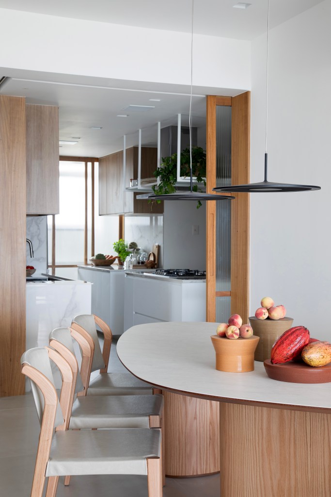 Apê tem ilha de cocção da cozinha com o cooktop voltado para o mar. Projeto de Rafael Ramos. Na foto, sala de jantar com mesa triangular, cadeiras, porta de correr para cozinha.