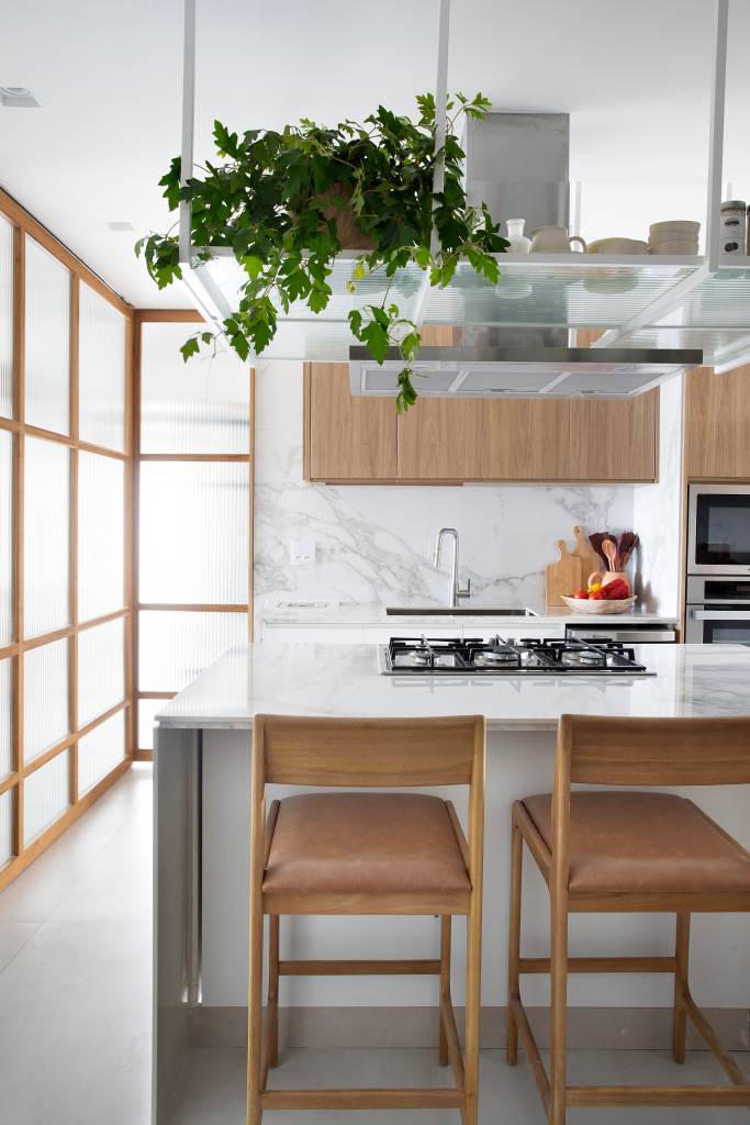 Apê tem ilha de cocção da cozinha com o cooktop voltado para o mar. Projeto de Rafael Ramos. Na foto, cozinha, bancada branca, backsplash marmorizado. banquetas.