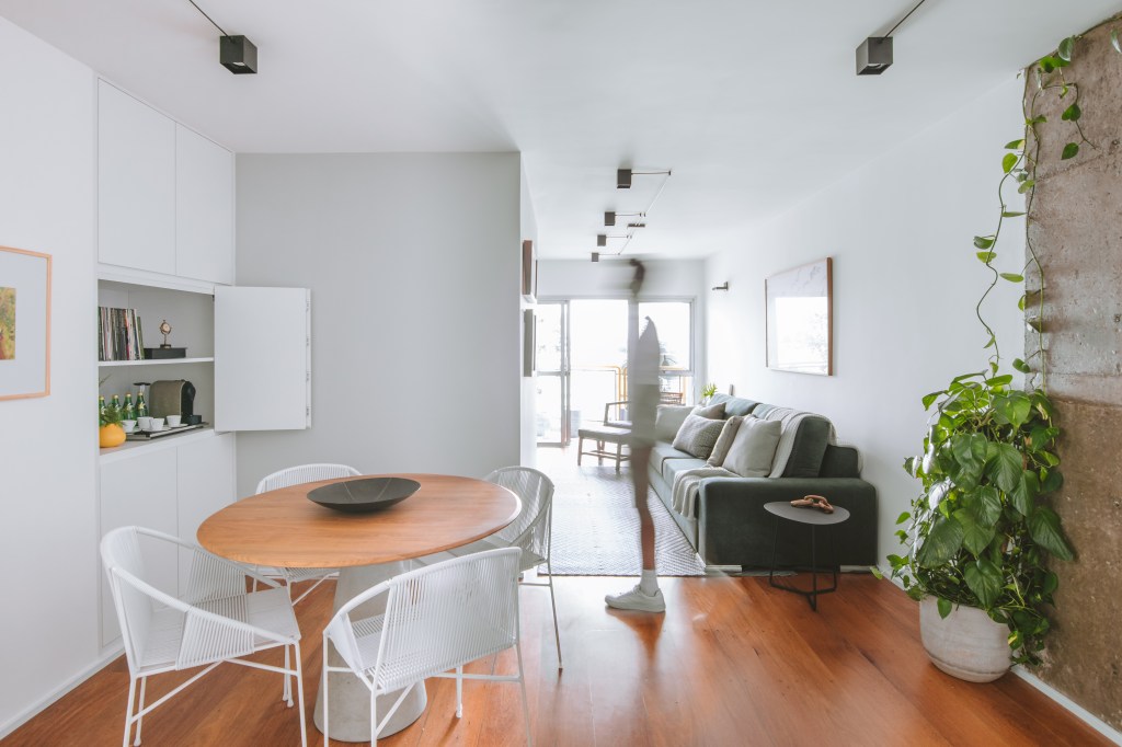 Apê industrial de 75 m² tem cozinha verde menta com bancada de cimento. Projeto de Rawi Arquitetura + Design. Na foto, sala de estar e jantar integradas, piso de madeira, sofá verde.