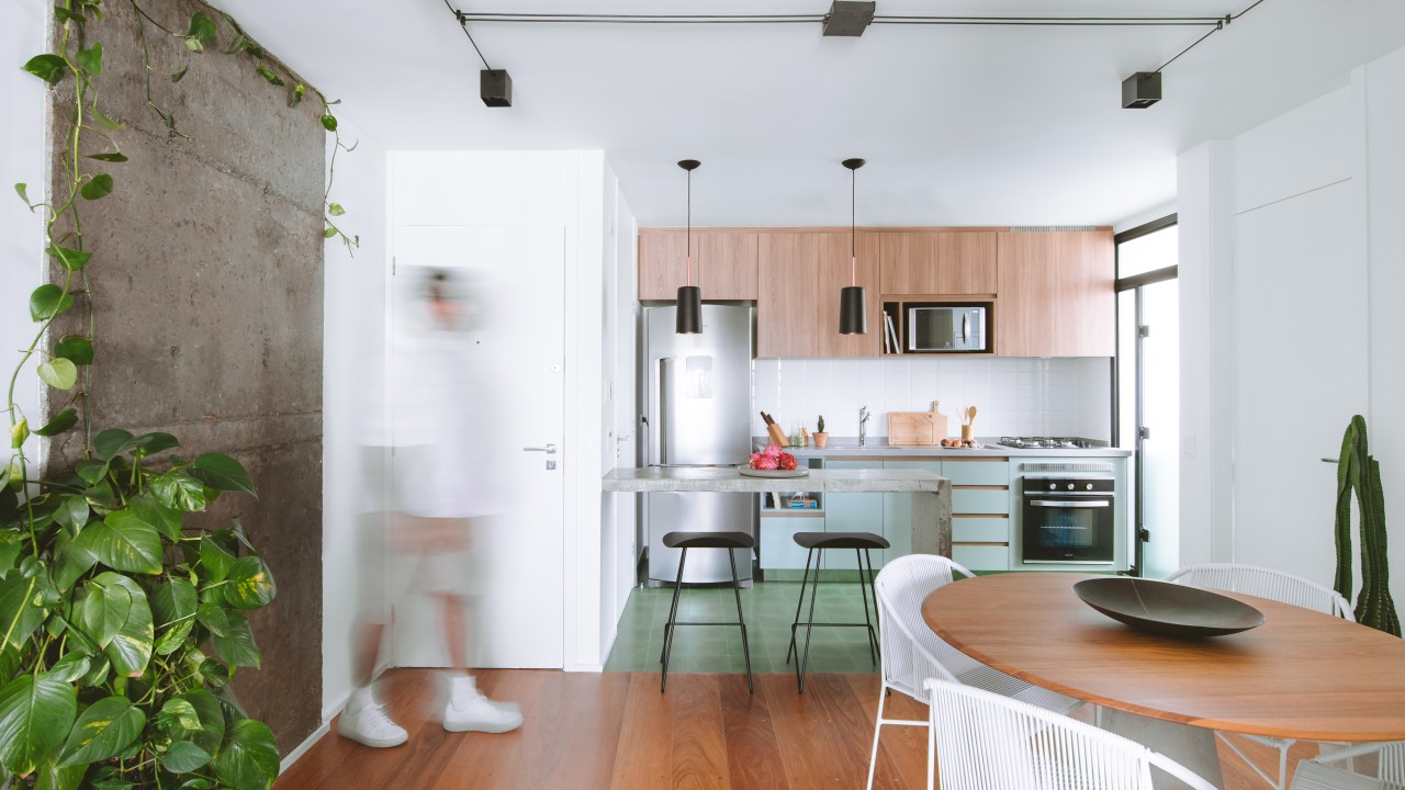 Apê industrial de 75 m² tem cozinha verde menta com bancada de cimento. Projeto de Rawi Arquitetura + Design. Na foto, sala de jantar, cadeiras brancas, piso de madeira.