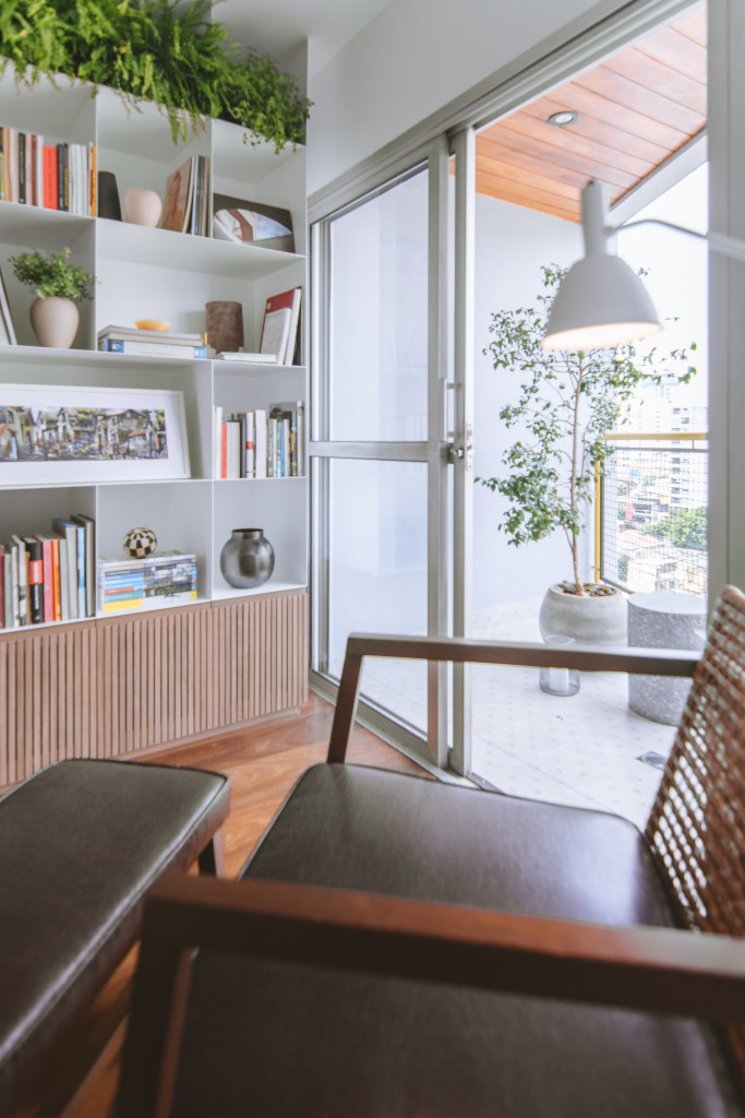 Apê industrial de 75 m² tem cozinha verde menta com bancada de cimento. Projeto de Rawi Arquitetura + Design. Na foto, cantinho de leitura, poltrona com pufe, luminária, estante com livros.