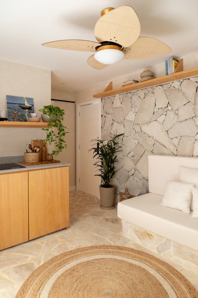 Apê térreo de 45 m² ganha cara de casa de praia com área externa integrada. Projeto de Casa Tauari. Na foto, sala de estar, parede de pedra, sofá branco, tapete redondo de fibra.