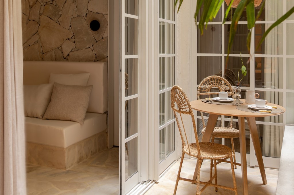 Apê térreo de 45 m² ganha cara de casa de praia com área externa integrada. Projeto de Casa Tauari. Na foto, quintal pequeno com palmeira, mesa redonda pequena, cadeiras, portas de correr de vidro.