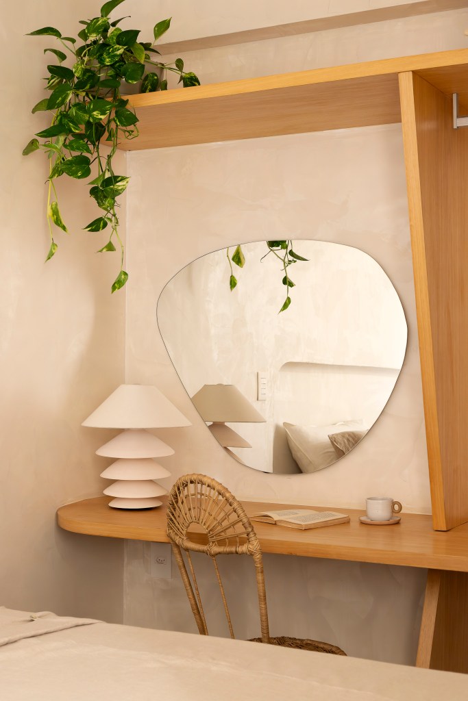 Apê térreo de 45 m² ganha cara de casa de praia com área externa integrada. Projeto de Casa Tauari. Na foto, quarto com penteadeira, espelho em formato orgânico, abajur branco.
