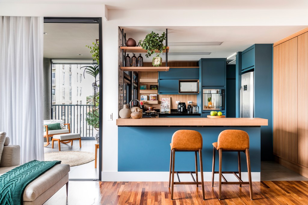 Azulejos estampados e cores trazem personalidade a apê de 100 m². Projeto de Carolina Munhoz. Na foto, cozinha integrada com a sala, parede azul, balcão e varanda.