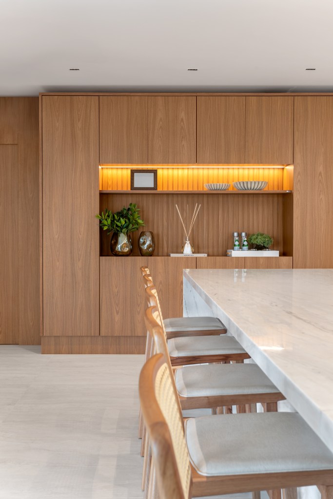 À beira-mar, apartamento de 160 m² traz uma estética clean e atemporal. Projeto de Mezzure Arquitetura. Na foto, sala de jantar com marcenaria, balcão e bancos.