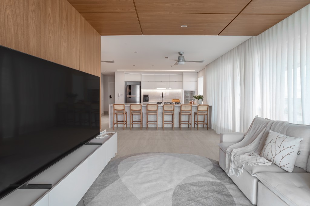 À beira-mar, apartamento de 160 m² traz uma estética clean e atemporal. Projeto de Mezzure Arquitetura. Na foto, sala integrada com cozinha, bancada e TV.