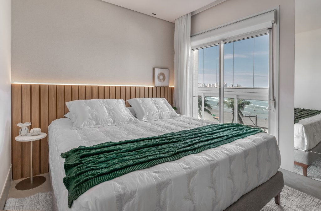 À beira-mar, apartamento de 160 m² traz uma estética clean e atemporal. Projeto de Mezzure Arquitetura. Na foto, quarto de casal com vista para o mar e cabeceira ripada.