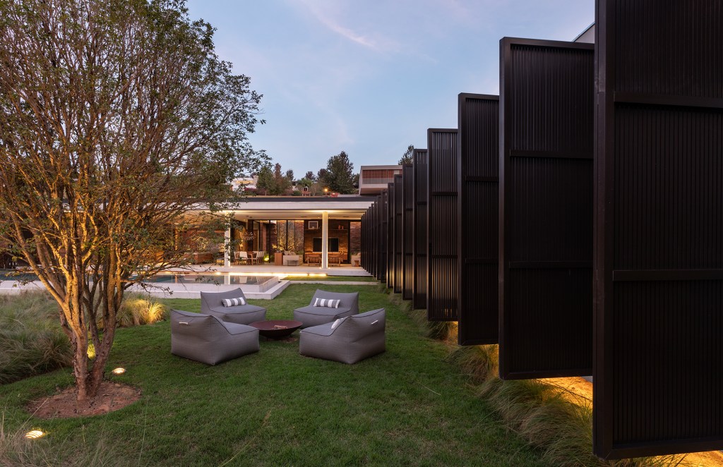 Brises metálicos dão movimento à fachada desta casa de 700 m². Projeto de Padovani Arquitetos. Na foto, jardim com firepit, brises e piscina.