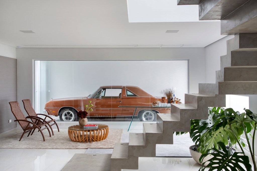 Casa ganha segundo andar e decoração inspirada no automobilismo. Projeto de Gabriel Fernandes. Na foto, sala de estar, abertura com vidro para carro na garagem.