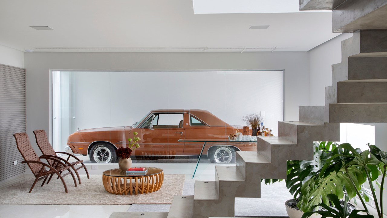 Casa ganha segundo andar e decoração inspirada no automobilismo. Projeto de Gabriel Fernandes. Na foto, sala de estar, abertura com vidro para carro na garagem.