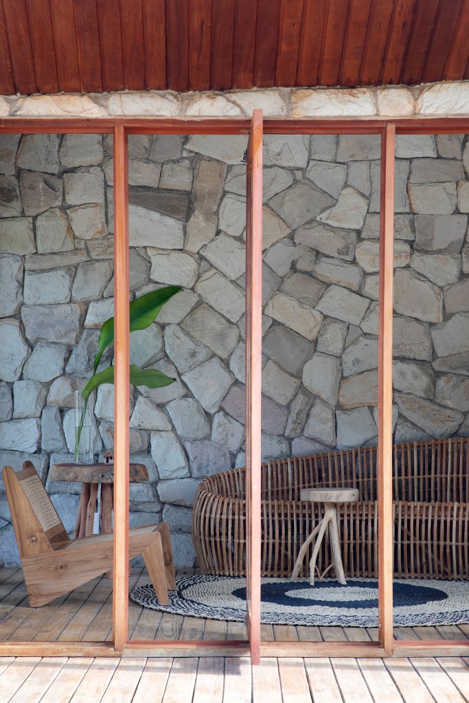 Chalé de praia de 60 m² tem decoração rústica e banheiro com claraboia. Projeto de Roby Macedo Arquitetura. Na foto, parede de pedra, brises verticais giratórios.