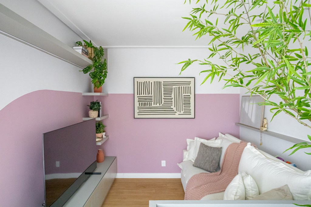 Cobertura tem espaço de armazenamento embaixo da escada e hidromassagem. Projeto de Go Up Arquitetura. Na foto, sala de estar, sofá branco, meia parede rosa, rack cinza, plantas.