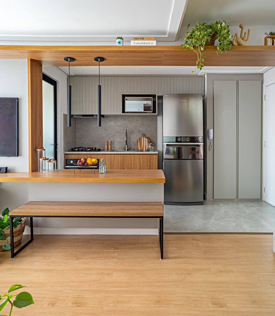 Cobertura tem espaço de armazenamento embaixo da escada e hidromassagem. Projeto de Go Up Arquitetura. Na foto, cozinha integrada, bancada de madeira, banco de madeira.