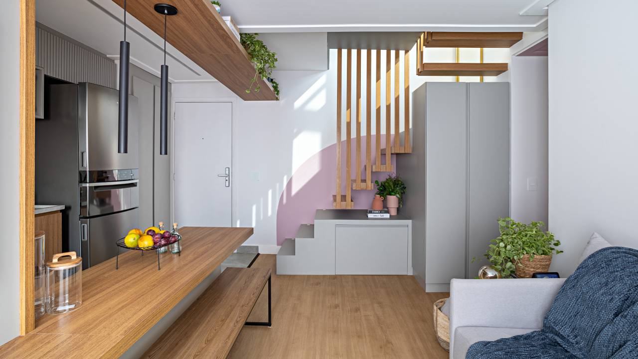 Cobertura tem espaço de armazenamento embaixo da escada e hidromassagem. Projeto de Go Up Arquitetura. Na foto, cozinha integrada, bancada de madeira, banco de madeira.