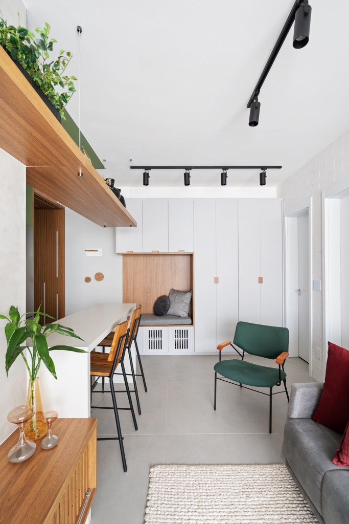 Com circulação otimizada, apê de 49 m² tem tons de verde e madeira. Projeto de Natalia Salla. Na foto, sala de estar, bancada de cozinha branca, cadeira verde, sapateira em marcenaria, trilho de spots.