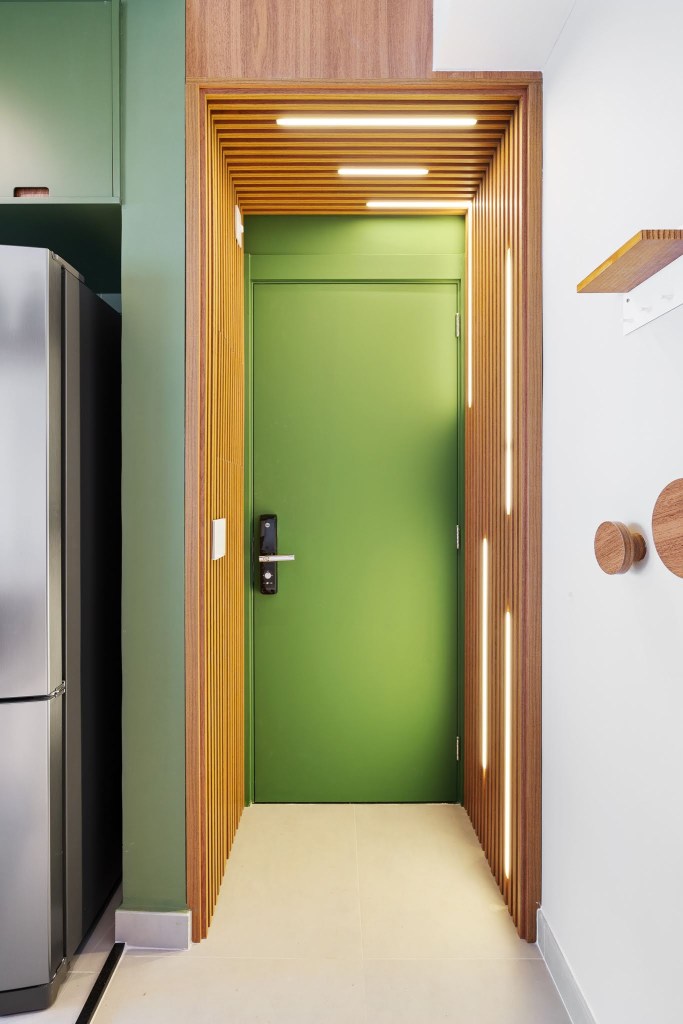 Com circulação otimizada, apê de 49 m² tem tons de verde e madeira. Projeto de Natalia Salla. Na foto, hall de entrada com porta verde, painéis de madeira com fitas de LED.