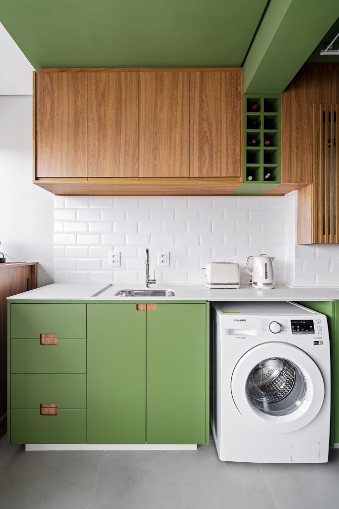Com circulação otimizada, apê de 49 m² tem tons de verde e madeira. Projeto de Natalia Salla. Na foto, lavanderia, bancada branca, máquina de lavar, armários verdes.