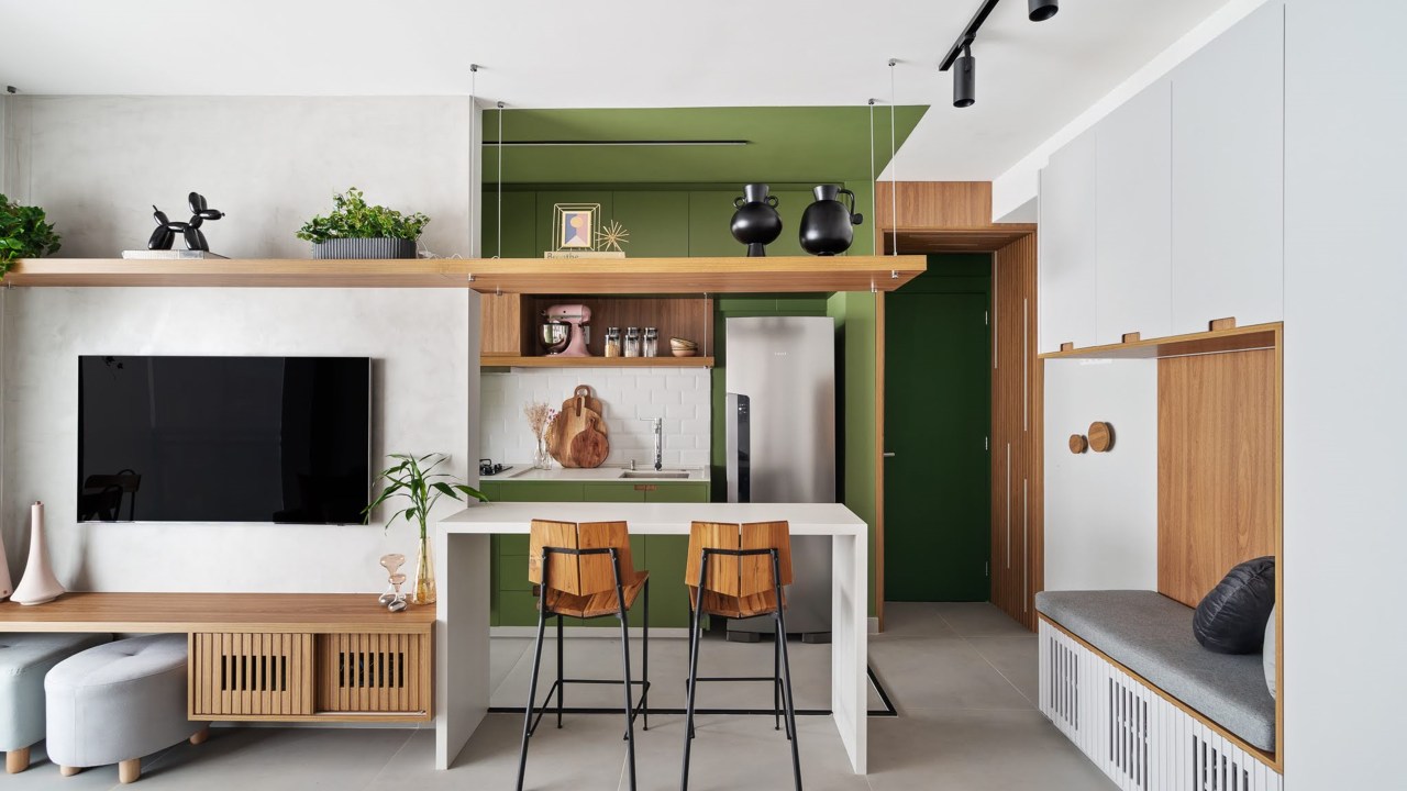 Com circulação otimizada, apê de 49 m² tem tons de verde e madeira. Projeto de Natalia Salla. Na foto, sala de estar integrada, sofá cinza, bancada branca, banquetas, cozinha. trilho de spots.