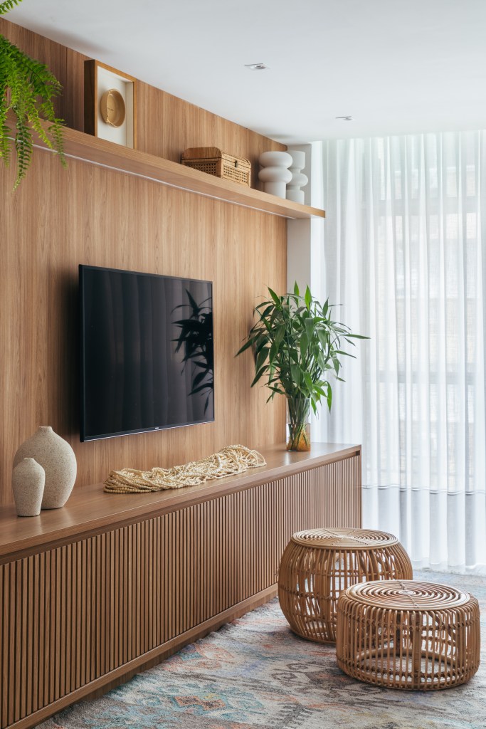 Dois apês viram um com cozinha gourmet, jantar e sala de TV integradas. Projeto de Fernanda Medeiros. Na foto, parede com painel de madeira, rack, cestos.