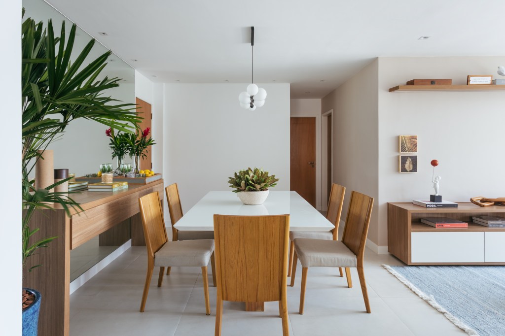 Dois apês viram um com cozinha gourmet, jantar e sala de TV integradas. Projeto de Fernanda Medeiros. Na foto, mesa com tampo branco laqueado, cadeiras, aparador.