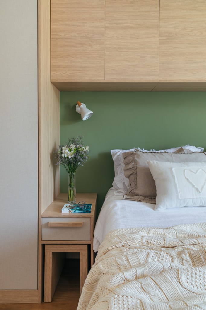 Dois apês viram um com cozinha gourmet, jantar e sala de TV integradas. Projeto de Fernanda Medeiros. Na foto, quarto de casal, marcenaria personalizada contornando a cama, parede verde.