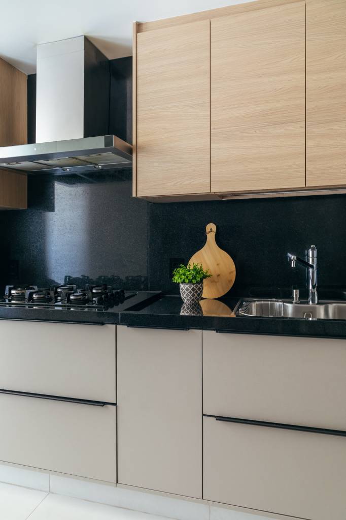 Dois apês viram um com cozinha gourmet, jantar e sala de TV integradas. Projeto de Fernanda Medeiros. Na foto, cozinha, bancada preta.