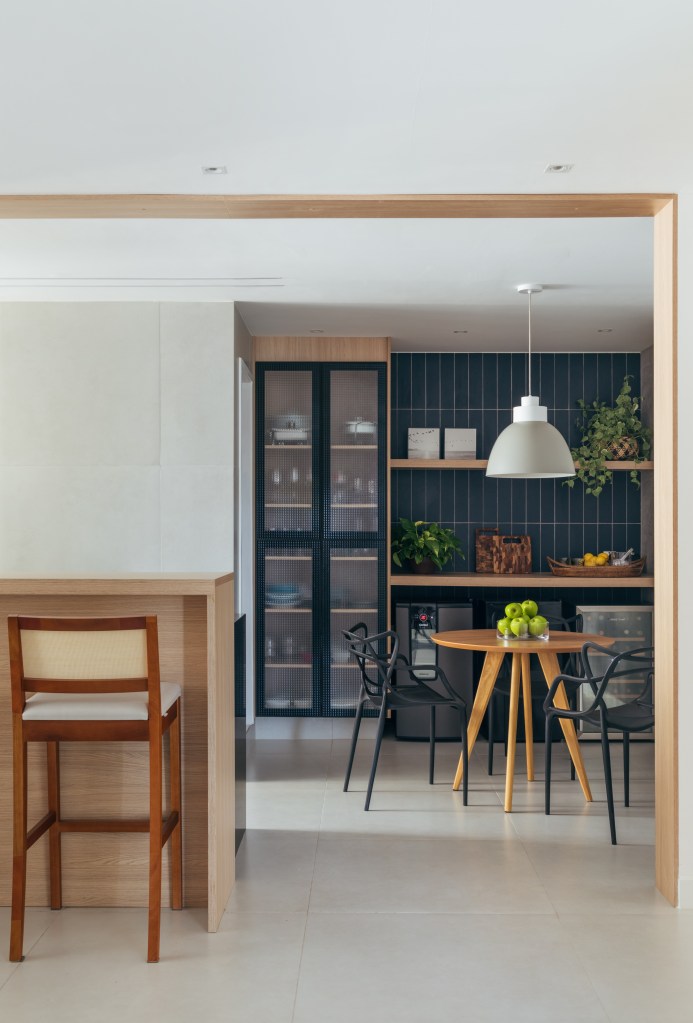 Dois apês viram um com cozinha gourmet, jantar e sala de TV integradas. Projeto de Fernanda Medeiros. Na foto, cozinha, parede de azulejos azuis, copa para refeições, mesa redonda pequena.
