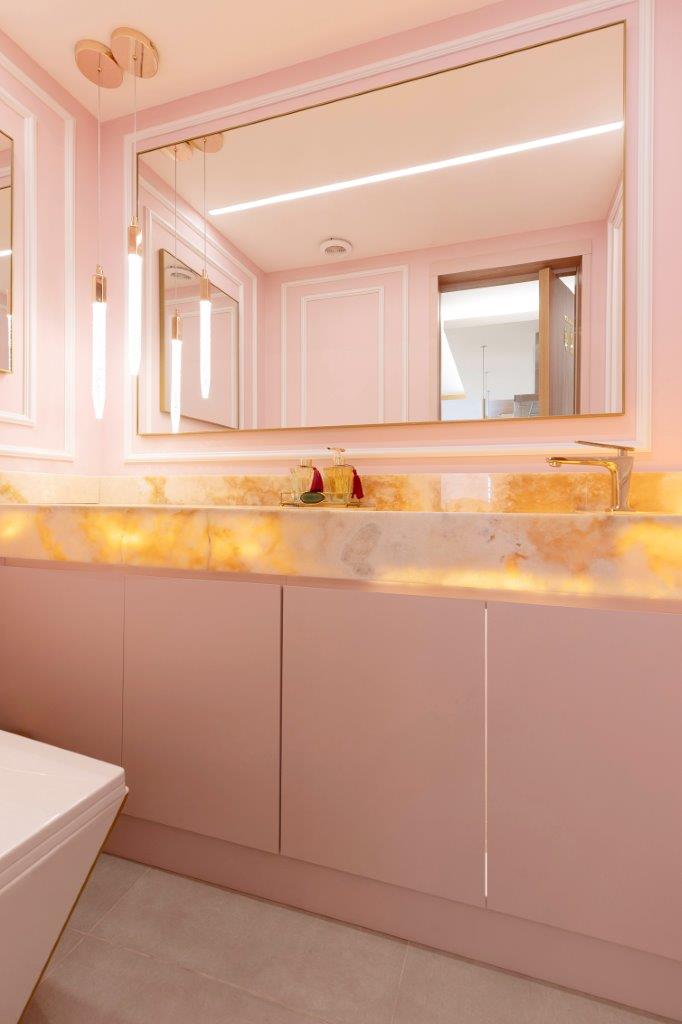 Dourado nos pendentes, serralheria e metais dão brilho à apê. Projeto de Marcela Rocca. Na foto, lavabo rosa, boiserie e bancada de ônix iluminada.