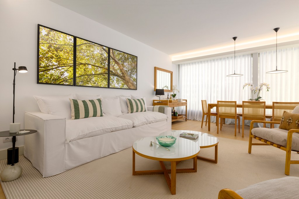 Feito à distância, apê de 160 m² em Portugal ganha décor com clima carioca. Projeto de C.W. Arquitetura. Na foto, sala de estar e jantar com quadros na parede, sofá e mesas.