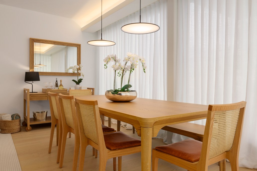 Feito à distância, apê de 160 m² em Portugal ganha décor com clima carioca. Projeto de C.W. Arquitetura. Na foto, sala de jantar com mesa de madeira e espelho.