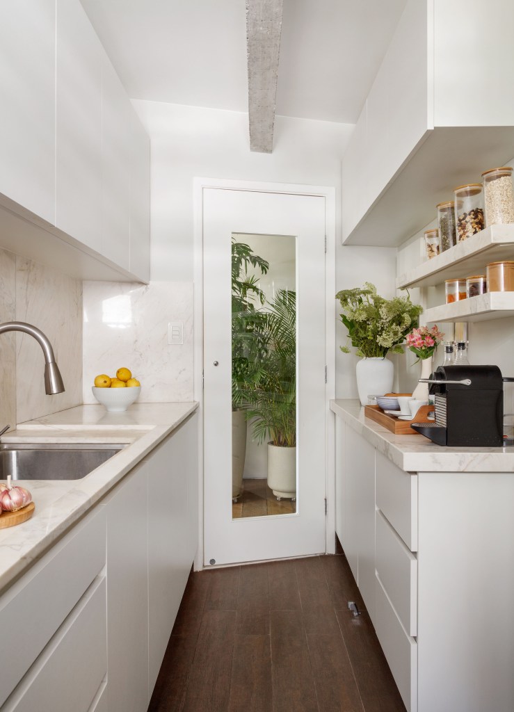 Mezanino é transformado em quarto nesta cobertura de 95 m². Projeto de DCC Arquitetura. Na foto, cozinha com armários brancos estreita.