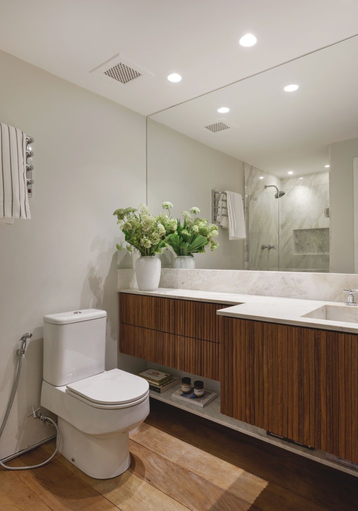 Mezanino é transformado em quarto nesta cobertura de 95 m². Projeto de DCC Arquitetura. Na foto, banheiro com bancada branca, marcenaria ripada, cuba esculpida.