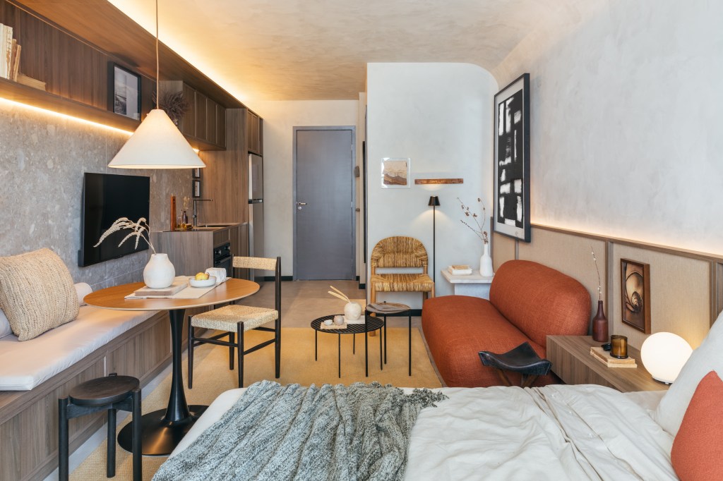 Mini loft de 28 m² ganha décor wabi-sabi com tons terrosos e minerais. Projeto de Studio Leandro Neves. Na foto, sala de estar, sofá em formato orgânico na cor terracota, cama de casal.