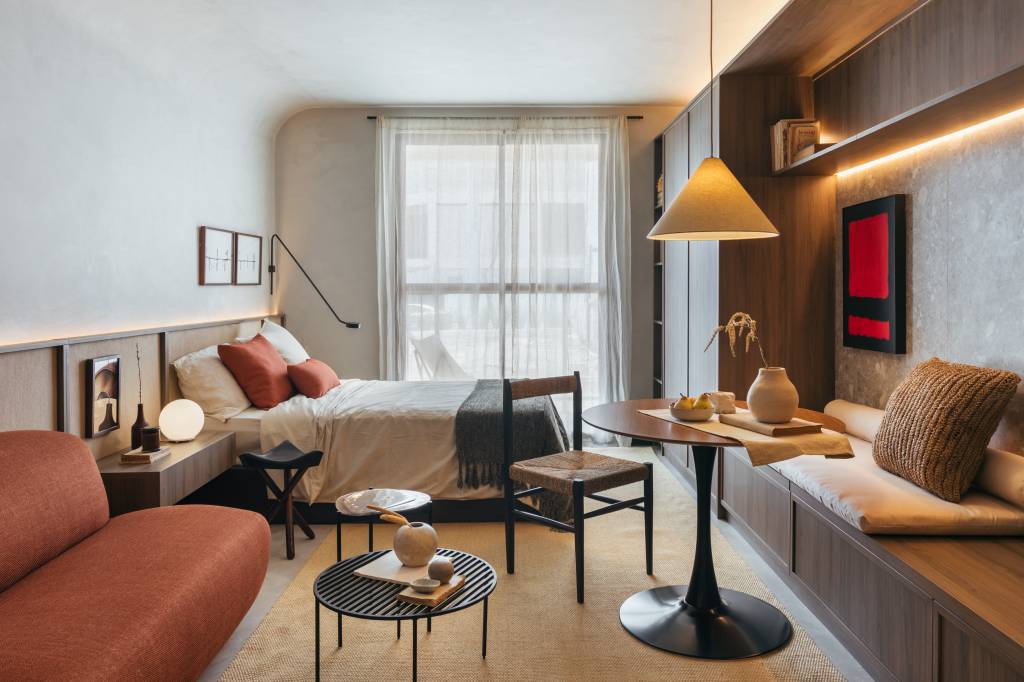 Mini loft de 28 m² ganha décor wabi-sabi com tons terrosos e minerais. Projeto de Studio Leandro Neves. Na foto, sala de estar, banco, mesa redonda pequena, luminária, cama de casal.