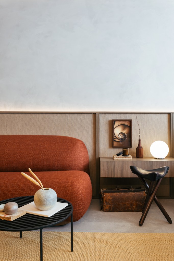 Mini loft de 28 m² ganha décor wabi-sabi com tons terrosos e minerais. Projeto de Studio Leandro Neves. Na foto, sala de estar, sofá curvo terracota, painel de madeira fazendo meia parede.