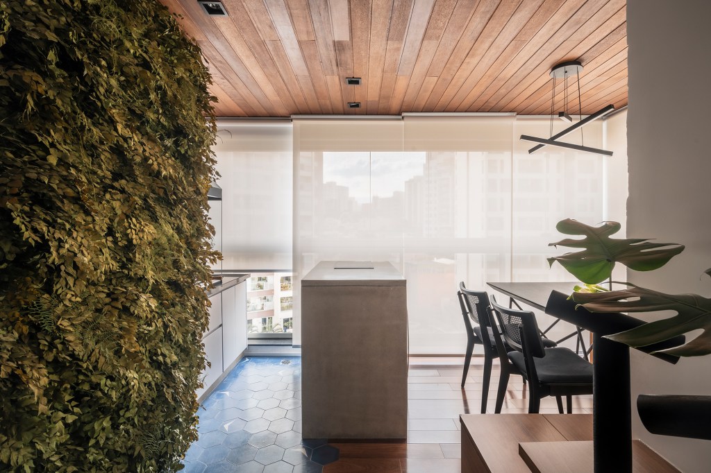Mix de elementos naturais e industriais marca décor deste apê de 67 m². Projeto de Box 14 Arquitetura. Na foto, varanda com ilha, banco e mesa de jantar.