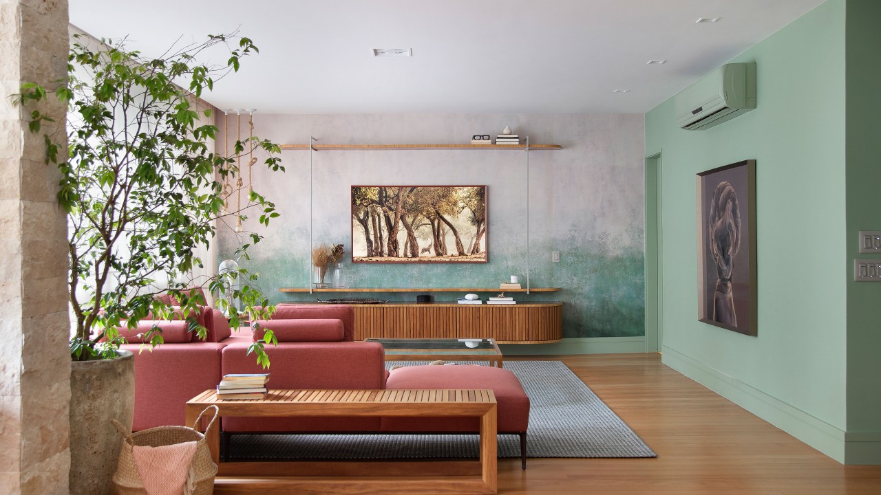 Papel de parede com efeito degradê envelhecido é destaque em área social. Projeto de Manoela Fleck. Na foto, sala de estar, plantas, sofá vermelho terroso.