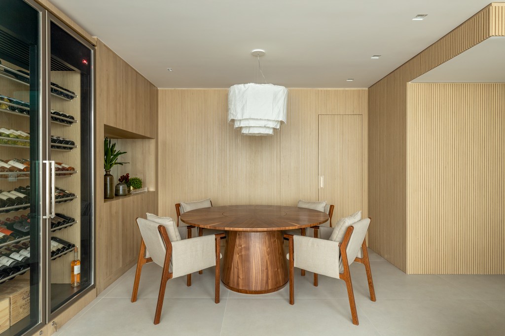Com pé-direito duplo, apê de 135 m² ganha novo quarto em reforma. Projeto de Camila Gazola e Stefania Pinheiro. Na foto, mezanino com adega, mesa de jantar, aparador e sofá.