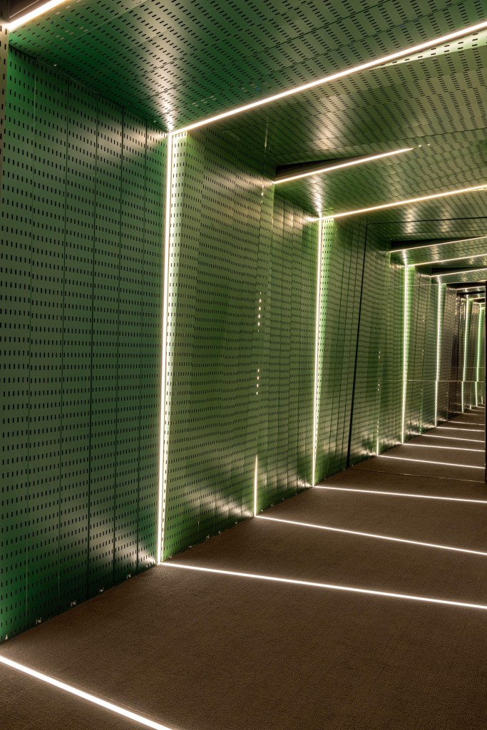 Projeto de escritório traz hall instagramável e árvore na sala de reuniões. Projeto de LAJ Arquitetura. Na foto, corredor, fitas de LED, painéis verdes vazados.