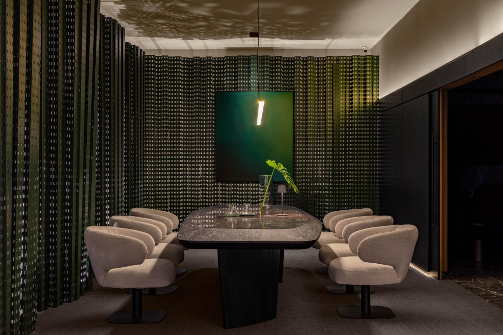 Projeto de escritório traz hall instagramável e árvore na sala de reuniões. Projeto de LAJ Arquitetura. Na foto, mesa de madeira preta, poltronas cinza, quadros verdes, painéis vazados verdes.