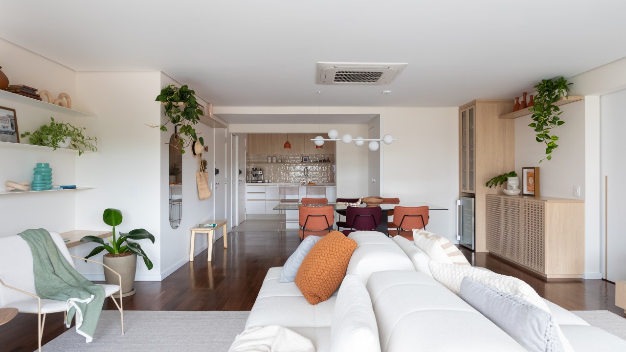 Reforma amplia living de apê de 100 m² com marcenaria planejada e plantas. Projeto de Estúdio Maré. Na foto, sala integrada, sofá ilha branco, cozinha integrada.