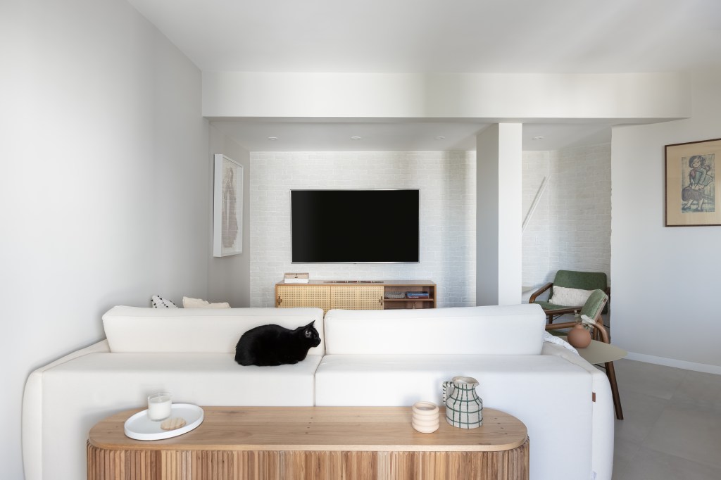 Reforma de apê cria lar prático e contemporâneo para casal e 4 gatinhos. Projeto de Estúdio Maré. Na foto, sala de estar, sofá branco, aparador atrás do sofá.