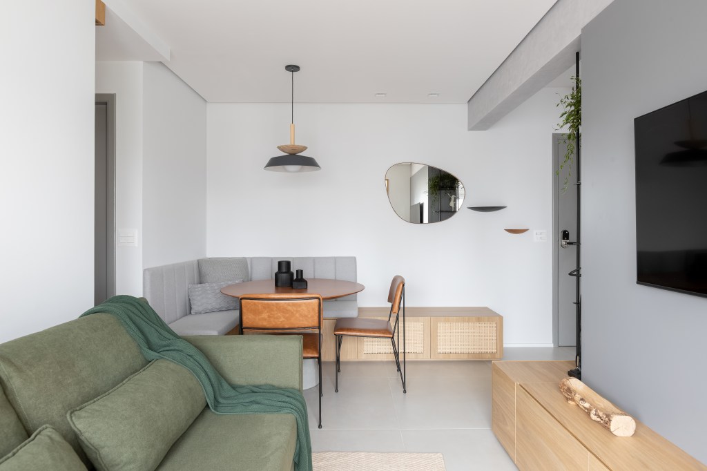 Reforma completa em apartamento de 56 m² cria décor em estilo Japandi. Projeto de Studio Monfré. Na foto, sala de estar e jantar, mesa redonda, rack de madeira, parede cinza com tv, sofá verde.