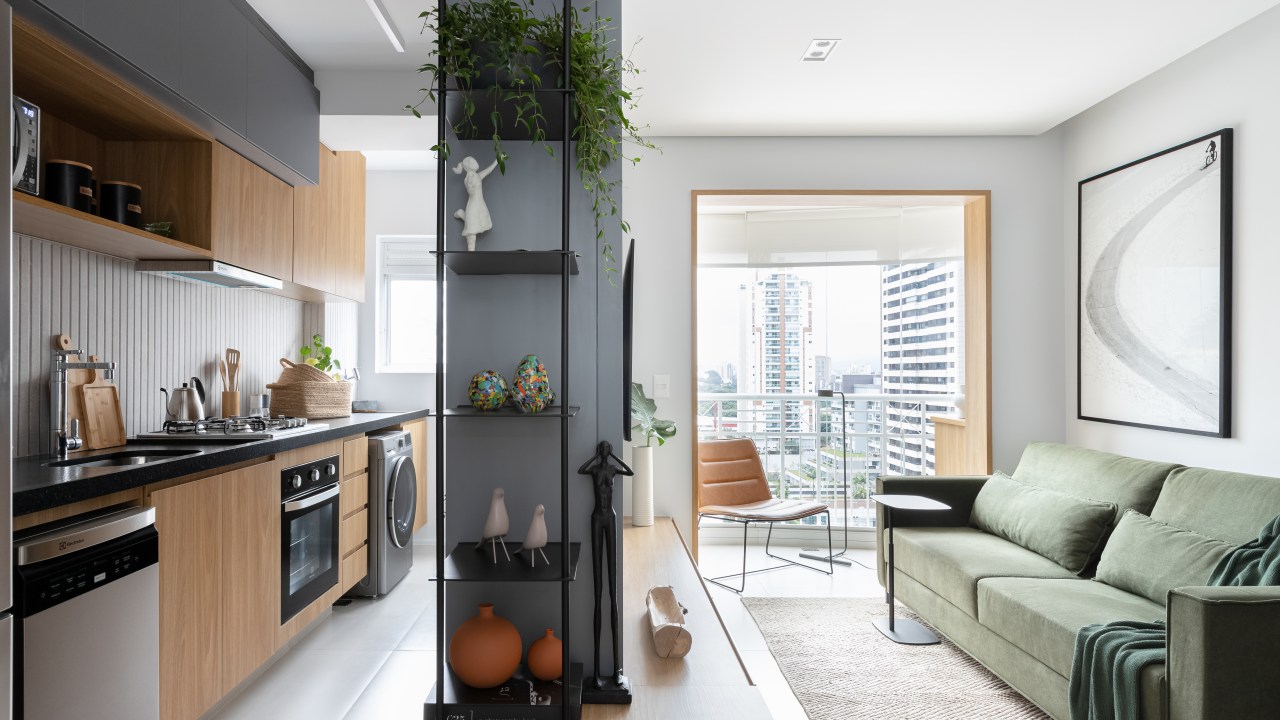 Reforma completa em apartamento de 56 m² cria décor em estilo Japandi. Projeto de Studio Monfré. Na foto, sala integrada com cozinha, sofá verde, parede cinza com tv.